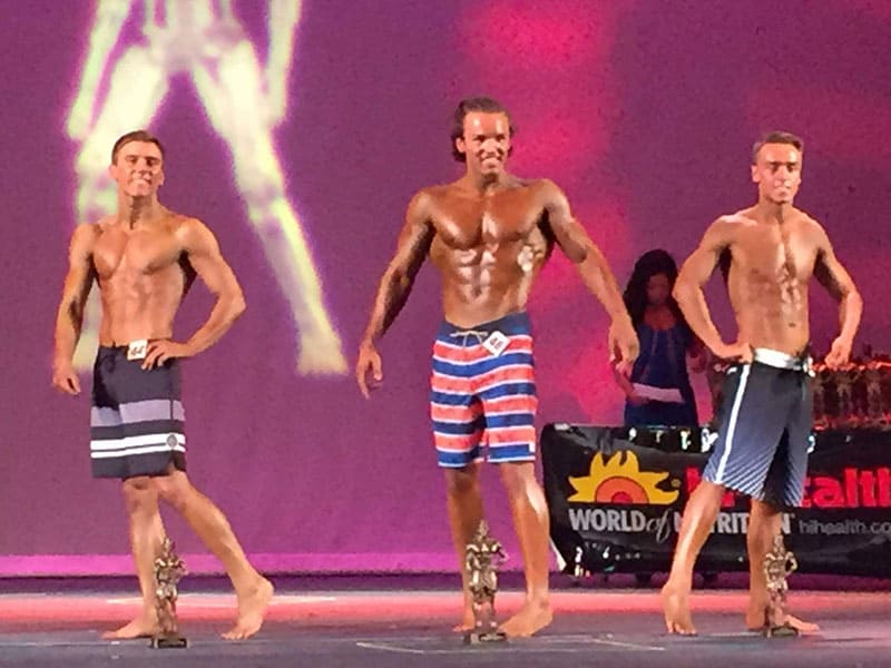 3 young male body builders competing on stage
